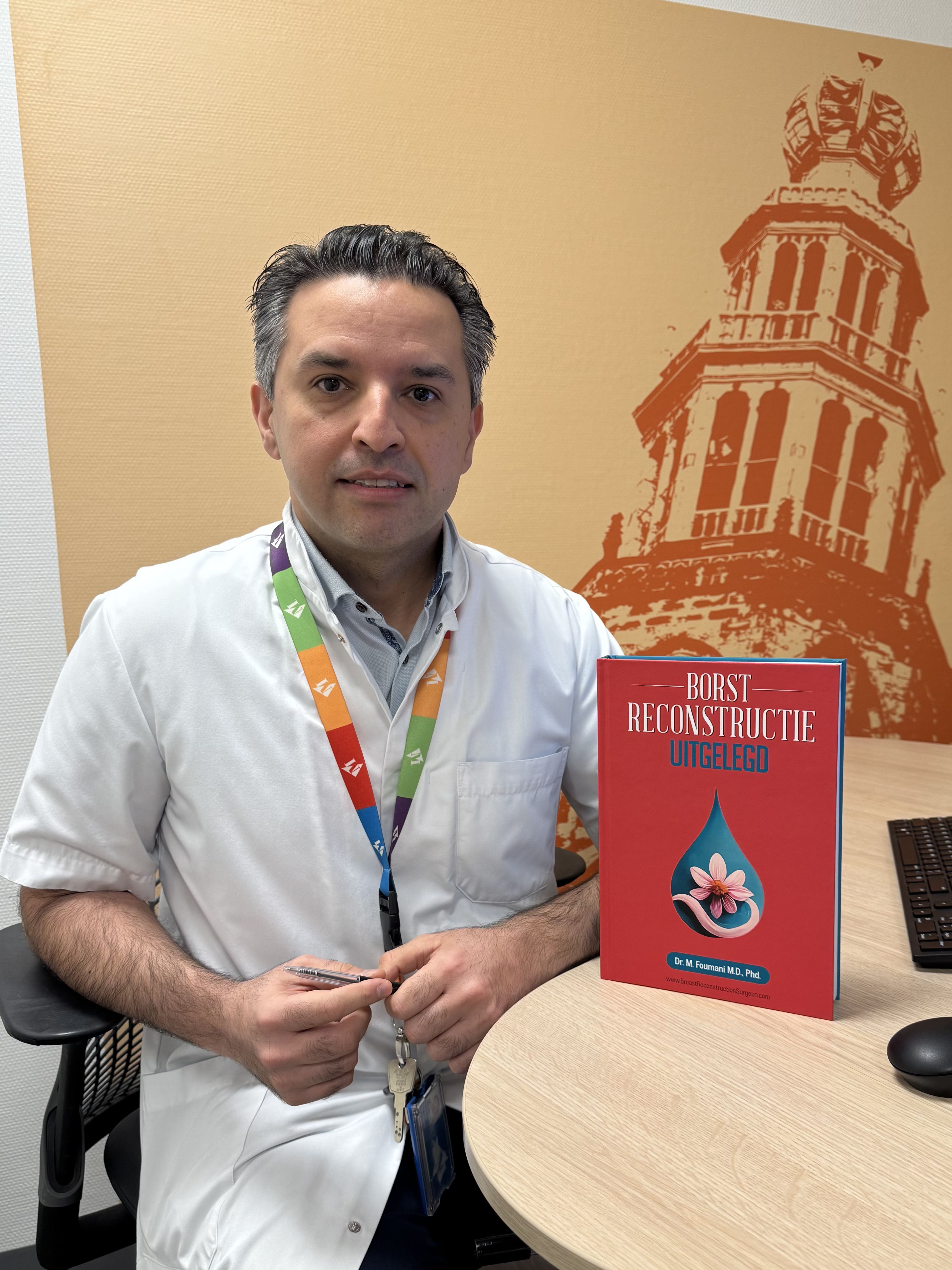 Plastisch chirurg Mahyar Foumani zit in de spreekkamer met zijn boek 'borstreconstructie uitgelegd'